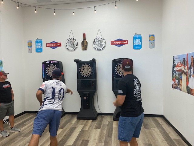 Players mid-throw at the electronic dartboards during a tournament