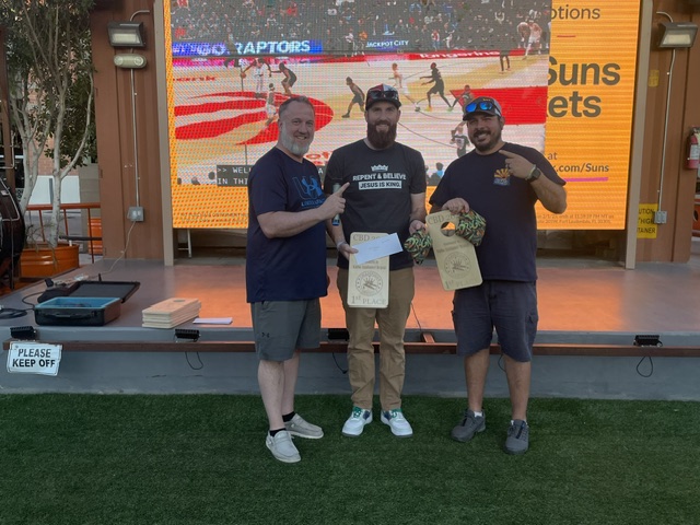 First-place cornhole champions pointing at their plaques