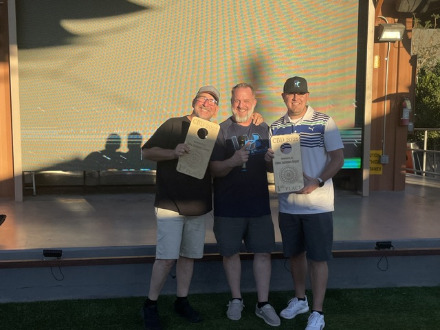 Smiling trio holding first-place plaques in golden light