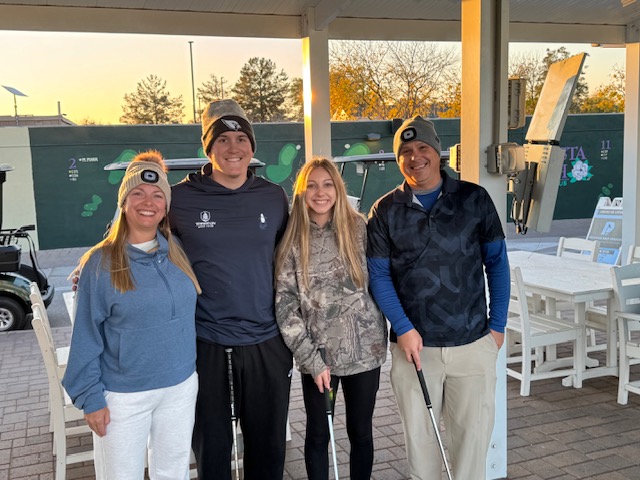 Smiling golf group in beanies at the driving range